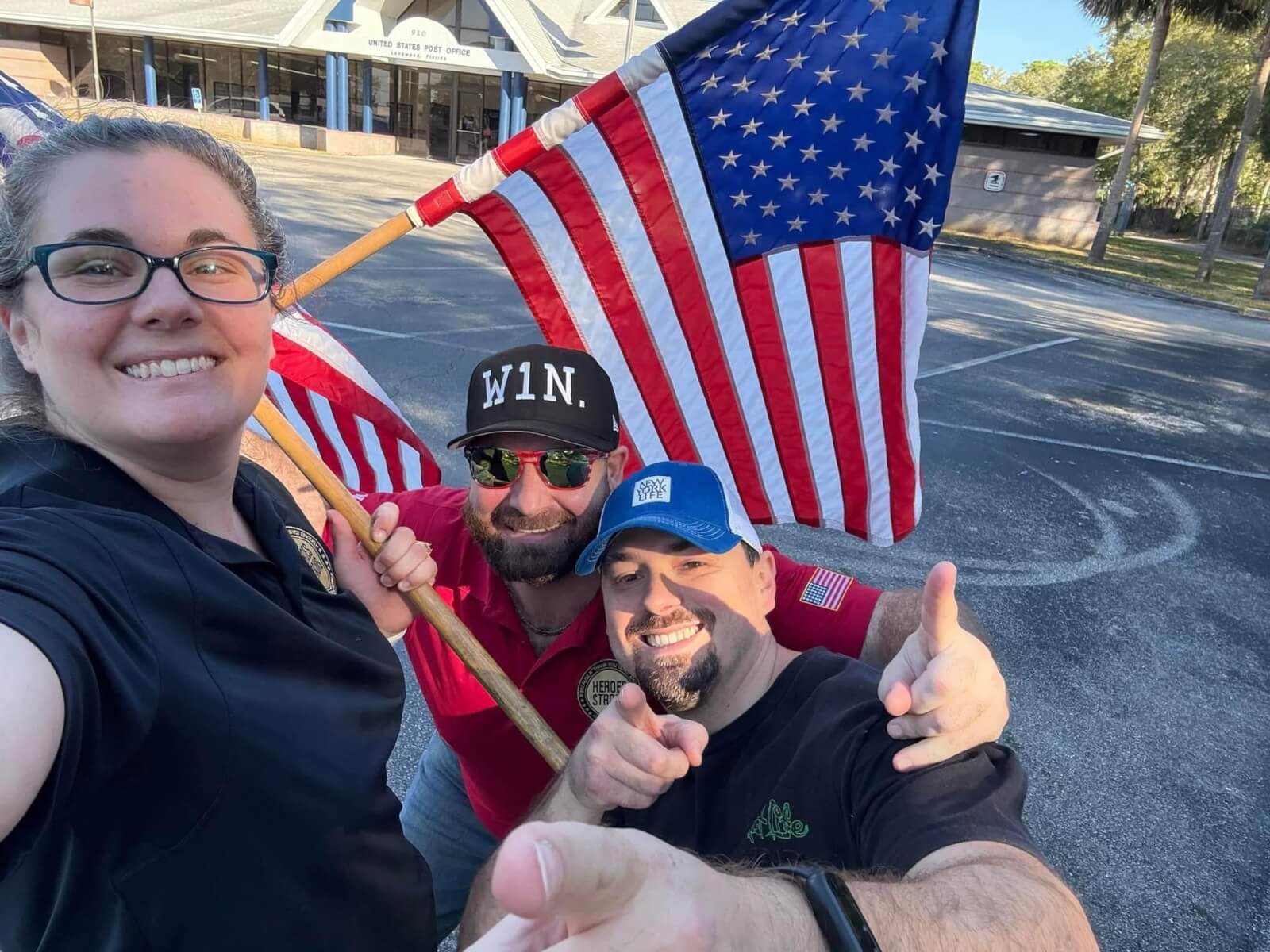Marine-spouse baker Megan Slaton with two Heroes Strong men as they mail care packages. American flag in the background.