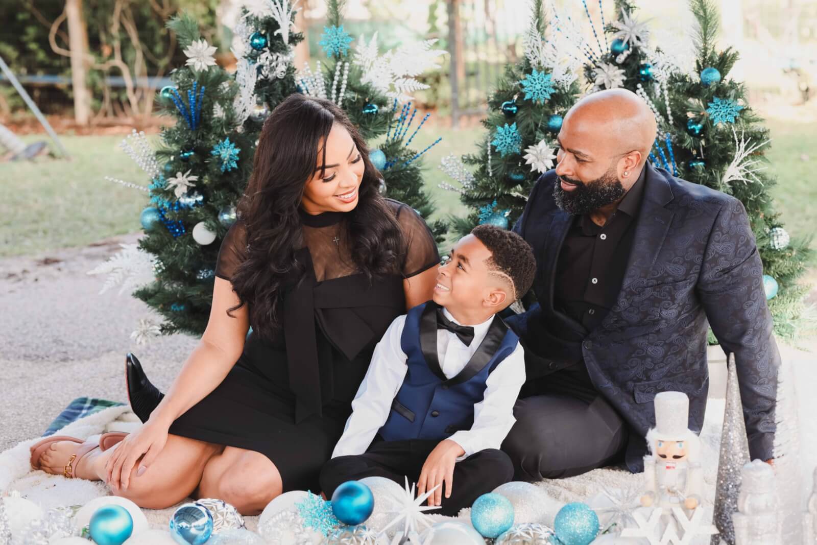 Toni Glaze, founder and president of family fashion brand Toni by Toni, gazes down at her son as her husband smiles at her in front of two Christmas trees decorated in blue and white.