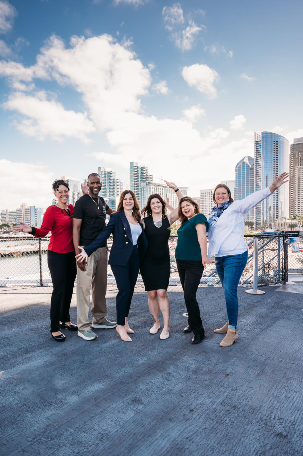 Successful business owners stand with arms outstretched in front of San Diego skyline. 