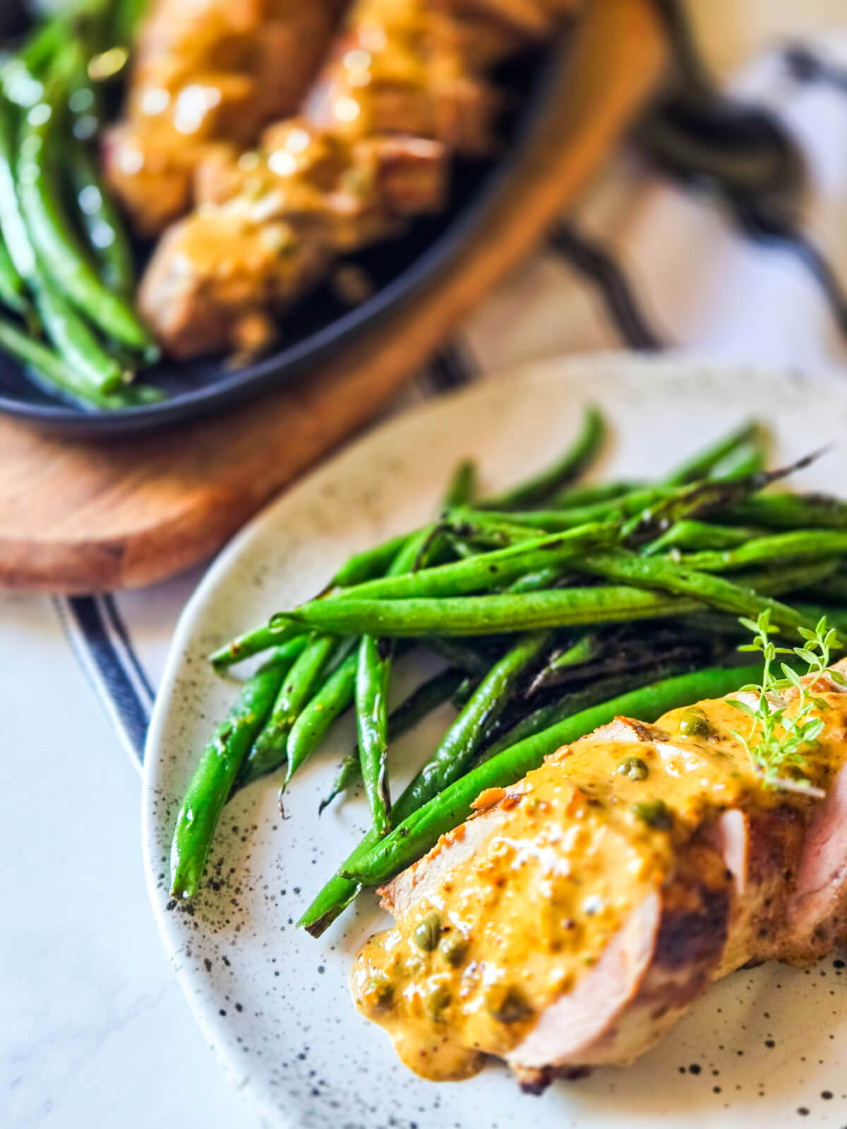 Holiday recipe Pork Tenderloin with a Creamy Mustard Sauce plated next to Seared Haricot Verts on a linen tablecloth.