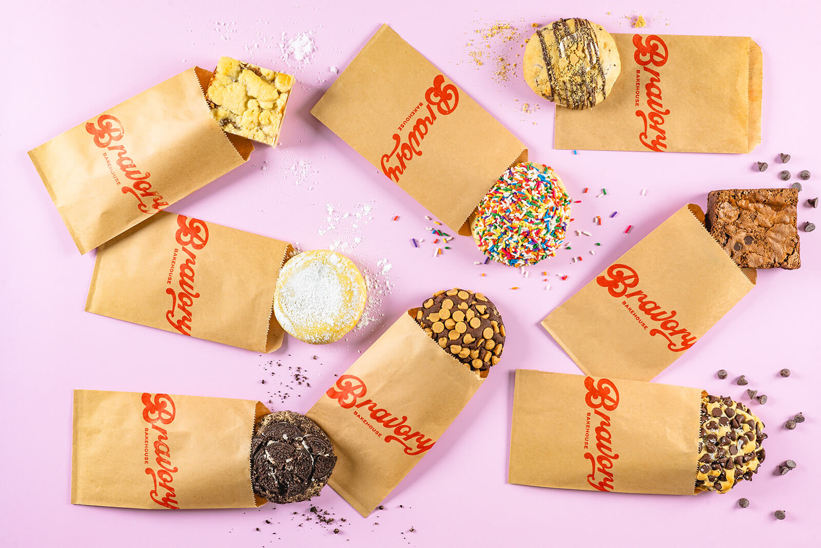 Variety of chocolate, sprinkle, and chocolate chip baked goods from Bravory Bakehouse, a military-owned small business, on a pink background.