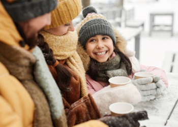 A happy young girl looking up at family while drinking hot cocoa during holiday getaway.