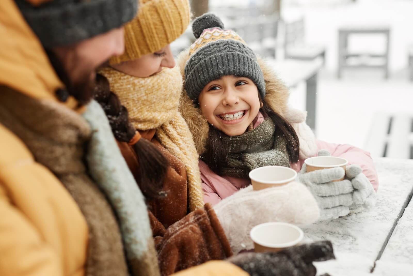 A happy young girl looking up at family while drinking hot cocoa during holiday getaway.