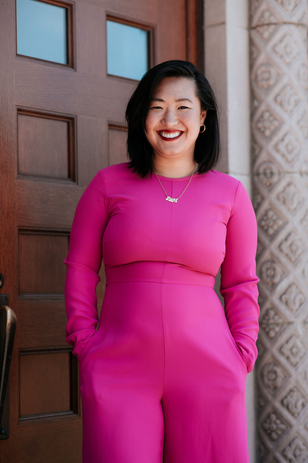 Yuzi Care Stephiney Foley stands smiling outside in a hot pink jumpsuit. 