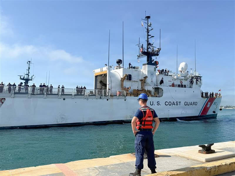 With backdrop of blue sky and on blue-green water, Coast Guard Cutter Mohawk approaches the pier at its homeport in Key West, Florida, as a Coast Guardsman stands on the pier and looks on.