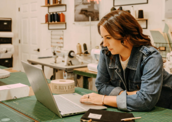 Lisa Bradley in an R. Riveter office with a laptop and canvas bag strewn on a wooden table with a cutting mat.