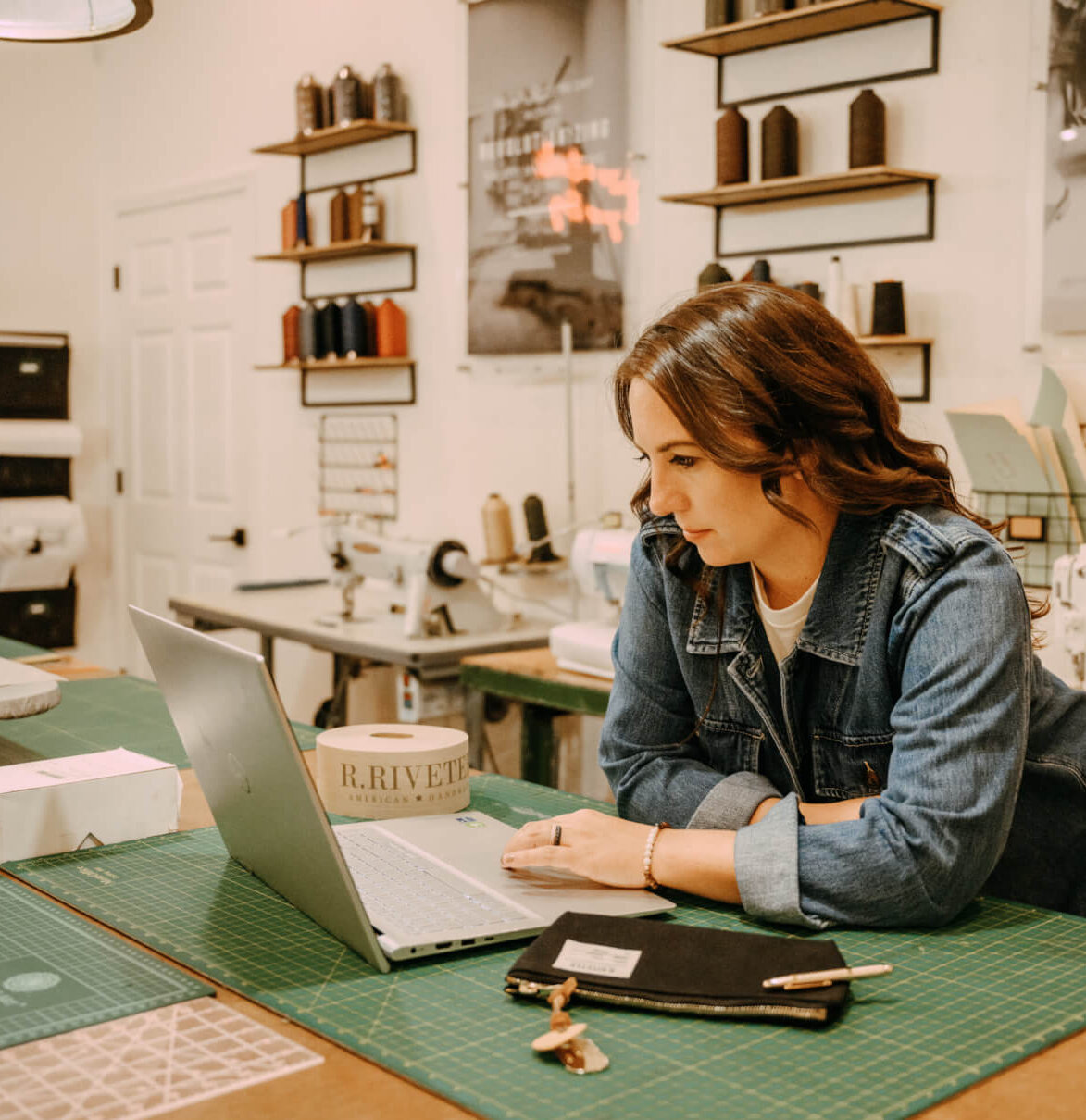 Lisa Bradley in an R. Riveter office with a laptop and canvas bag strewn on a wooden table with a cutting mat.