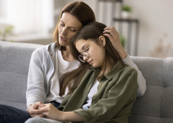 Mother talking to her young teen on couch while hugging her.