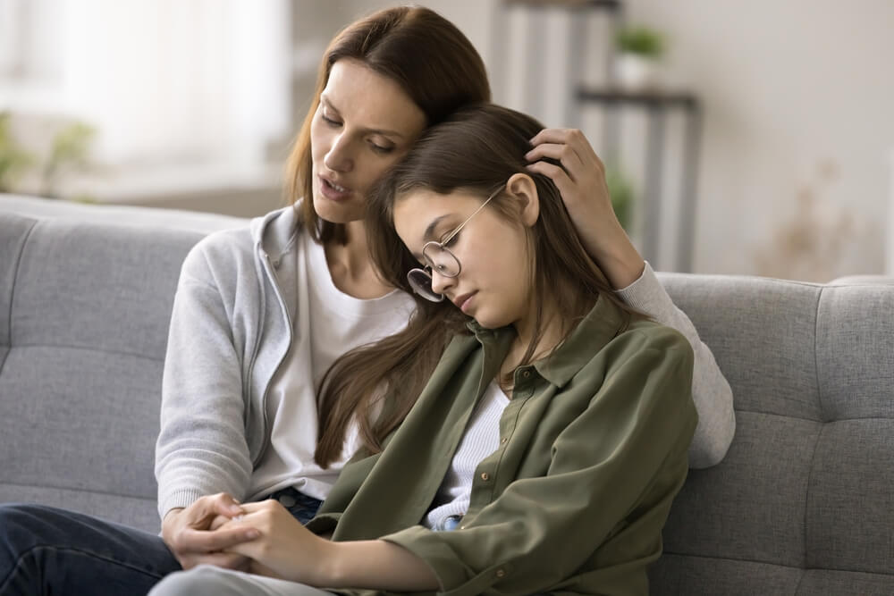 Mother talking to her young teen on couch while hugging her.