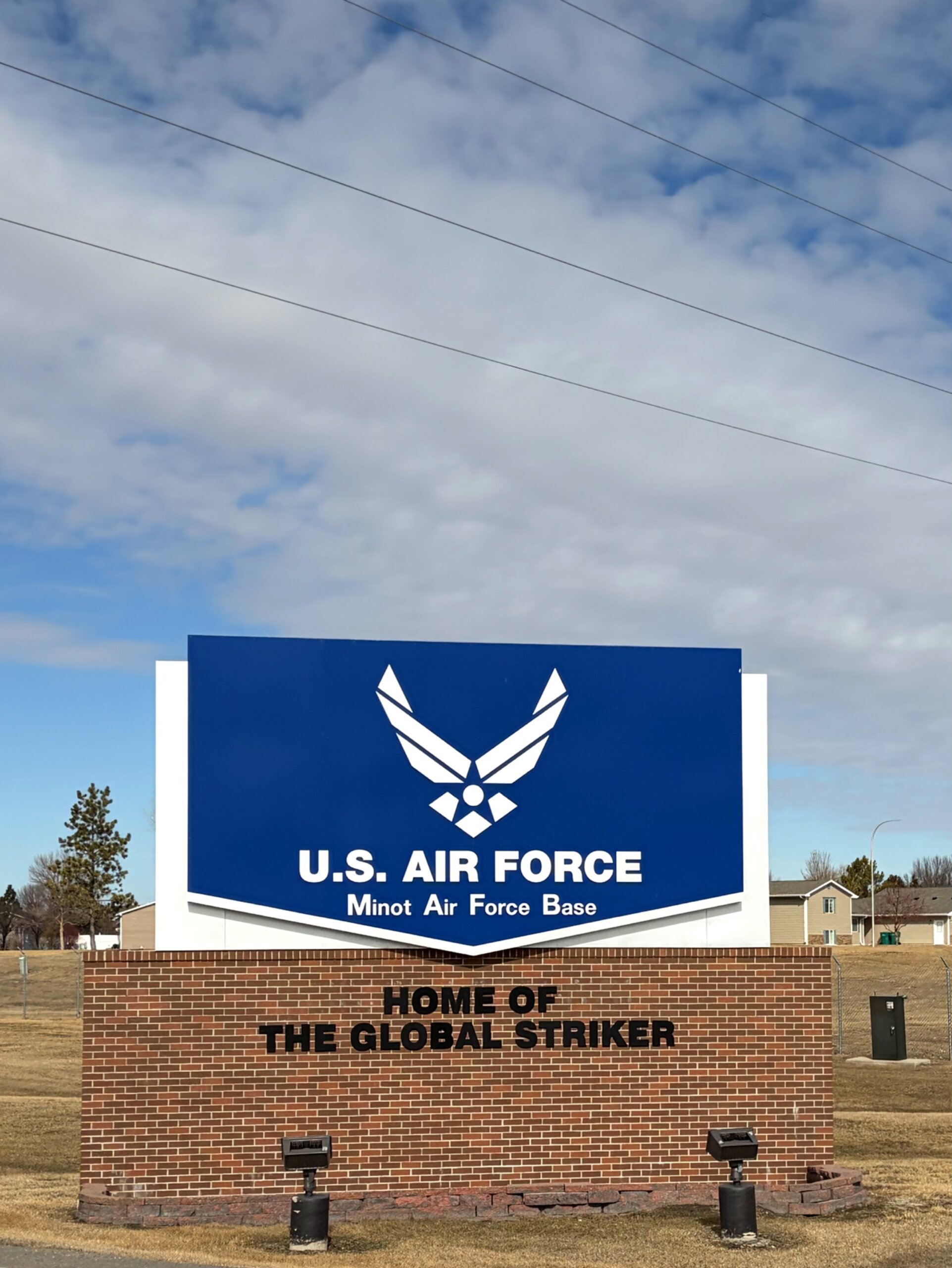 Set against a blue sky with white clouds, the blue Minot Air Force Base sign welcomes visitors to the installation. 