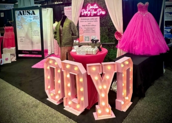 Operation Deploy Your Dress booth with large pink ODYD letters lit up with lights, with pink curtains and a pink dress in the background.