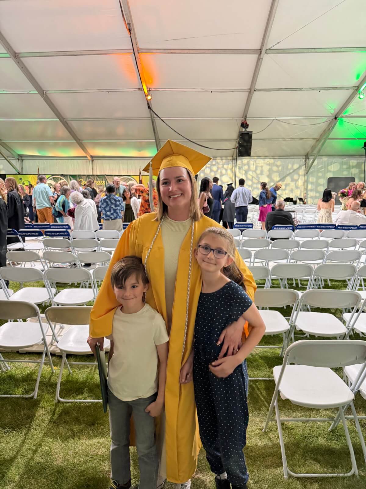 The author stands in her yellow cap and gown at her college graduation with her two young children.