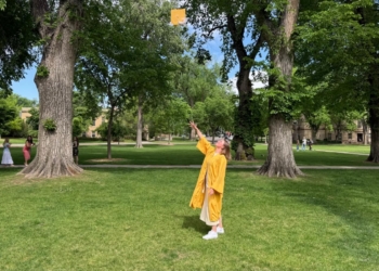 The author dressed in a yellow graduation gown tosses her yellow cap in the air after the graduation ceremony.