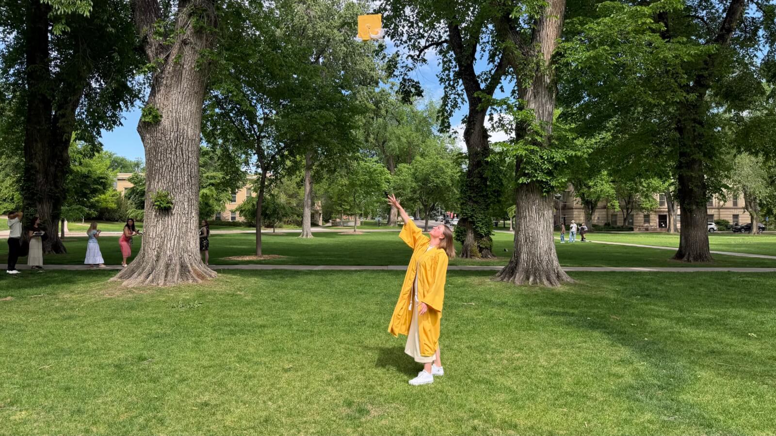 The author dressed in a yellow graduation gown tosses her yellow cap in the air after the graduation ceremony.